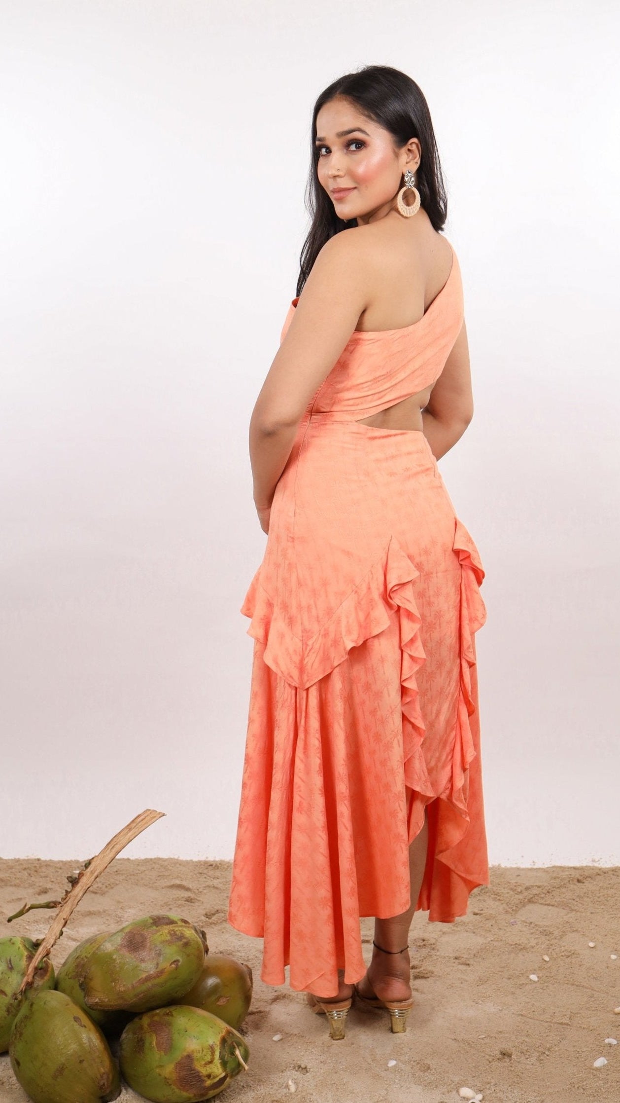 Woman wearing a orange color, one shoulder dress called Ibiza Dress By Soliesse with handkerchief hem. Beautiful waist cut out & ruffle details. Perfect outfit for a summer getaway or beach vacation.