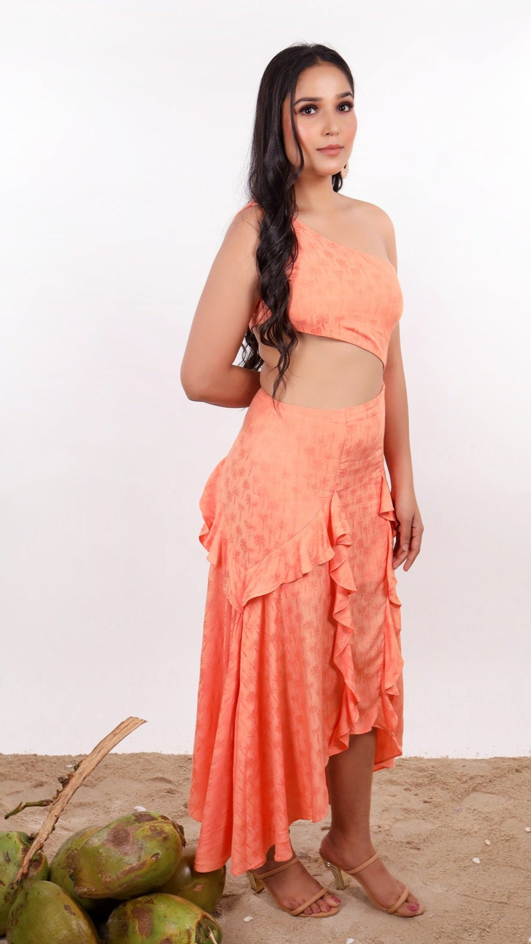 Woman wearing a orange color, one shoulder dress called Ibiza Dress By Soliesse with handkerchief hem. Beautiful waist cut out & ruffle details. Perfect outfit for a summer getaway or beach vacation.