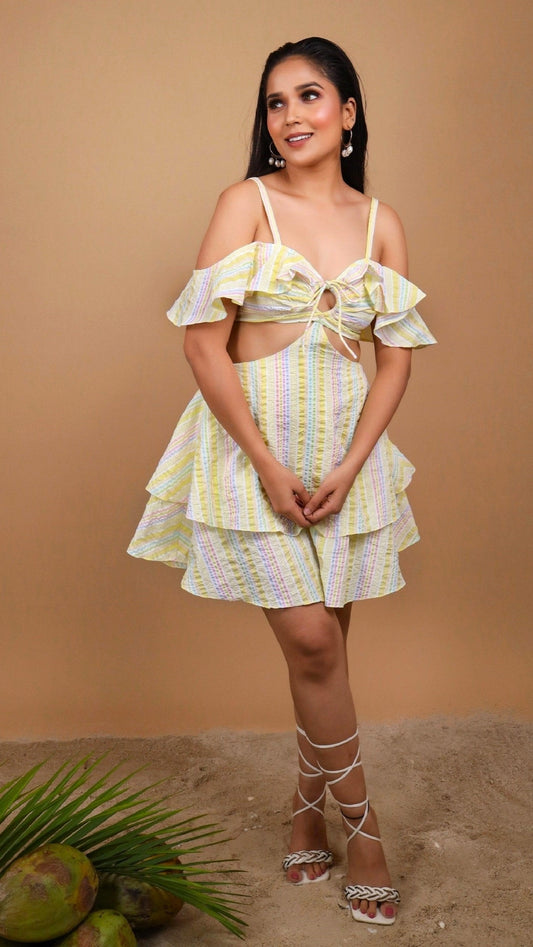 Woman sitting on a wicker chair holding a coconut against a beige background wearing an offshoulder yellow color striped dress by Soliesse. Its a perfect dress for a sunny day, brunch, date, a vacation or getaway. Its chic & comfortable at the same time.