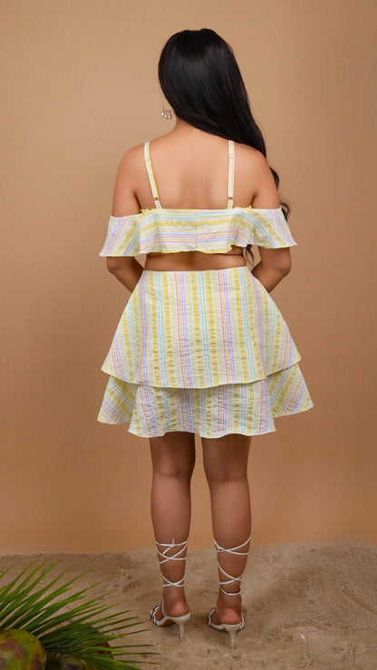 Woman posing against a beige background , back view, wearing an off shoulder yellow color striped dress by Soliesse. Its a perfect dress for a sunny day, brunch, date, a vacation or getaway. Its chic & comfortable at the same time.